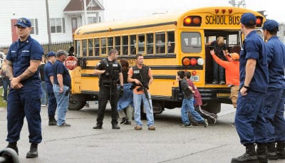 STUDENTS from the Eastport Elementary School are helped off the back of a school bus to run to a secure location, as armed law enforcement and Coast Guard personnel guard the site, after a t