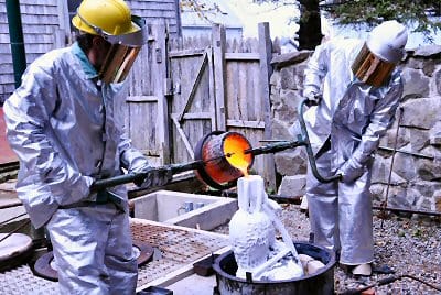 POURING molten bronze into the shell mold for a section of the mermaid sculpture to be placed on the Eastport seawall are Bill Labbadia (left) and Dick Klyver. The casting was carried out at
