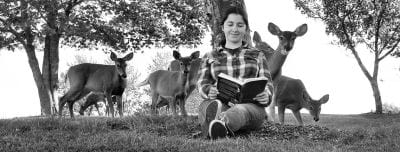 READING to a group of deer while sitting under an Eastport tree is Kathleen Esposito. (Don Dunbar photo)